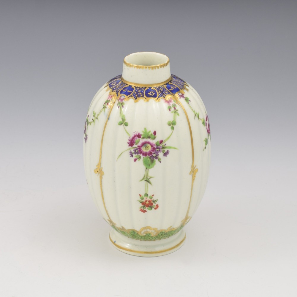 An 18th-century fluted white porcelain tea canister decorated with hand-painted floral swags, gilded trim, and a cobalt blue pattern around the neck.