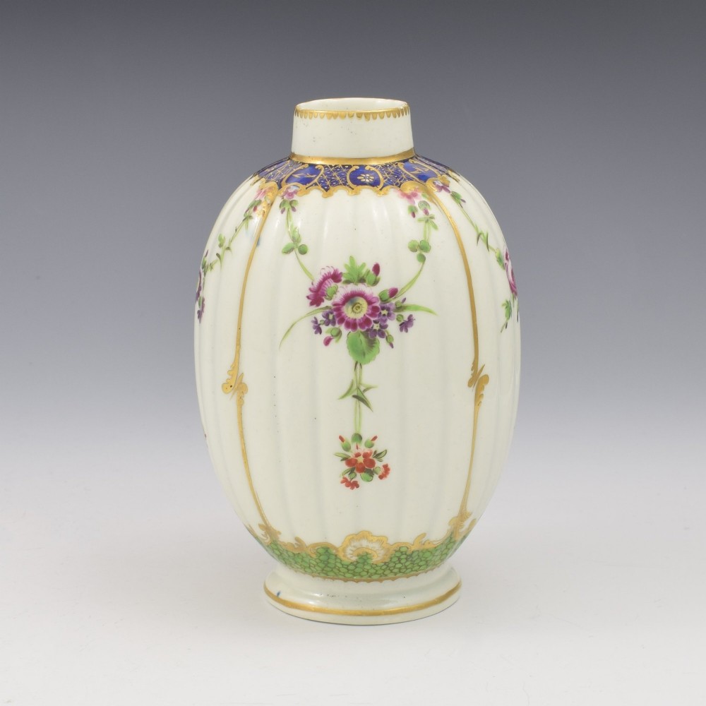 An 18th-century fluted white porcelain tea canister decorated with hand-painted floral swags, gilded trim, and a cobalt blue pattern around the neck. View II