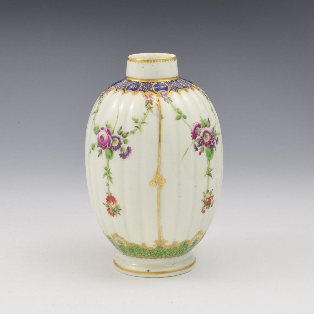 An 18th-century fluted white porcelain tea canister decorated with hand-painted floral swags, gilded trim, and a cobalt blue pattern around the neck. View V
