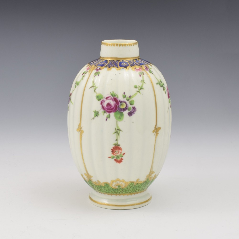 An 18th-century fluted white porcelain tea canister decorated with hand-painted floral swags, gilded trim, and a cobalt blue pattern around the neck. View VI