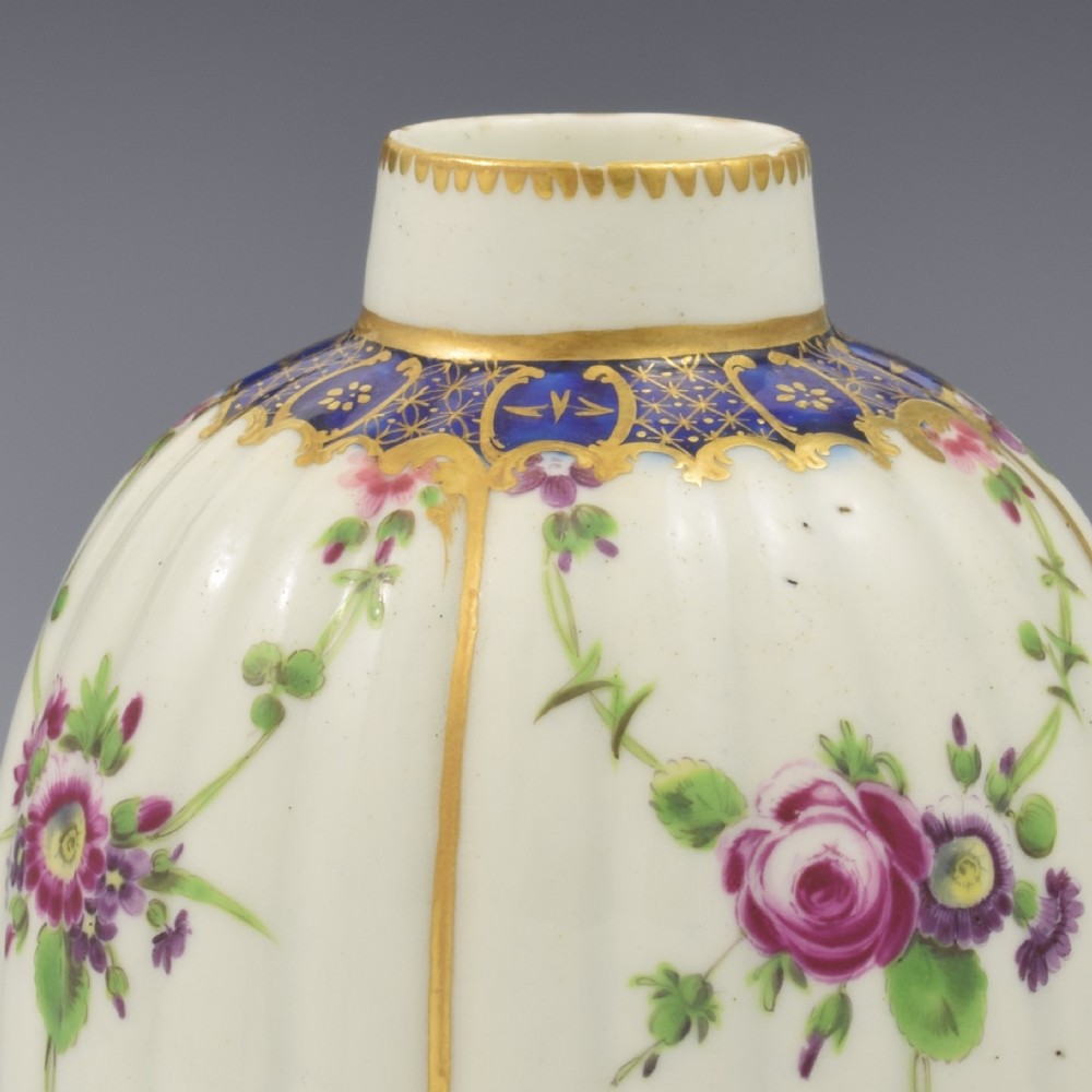 An 18th-century fluted white porcelain tea canister decorated with hand-painted floral swags, gilded trim, and a cobalt blue pattern around the neck. View IX