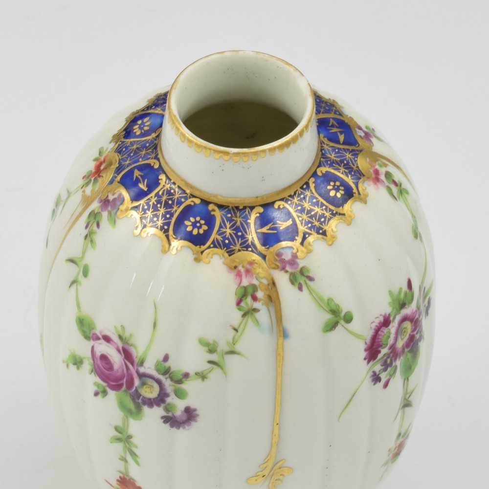 An 18th-century fluted white porcelain tea canister decorated with hand-painted floral swags, gilded trim, and a cobalt blue pattern around the neck. View X