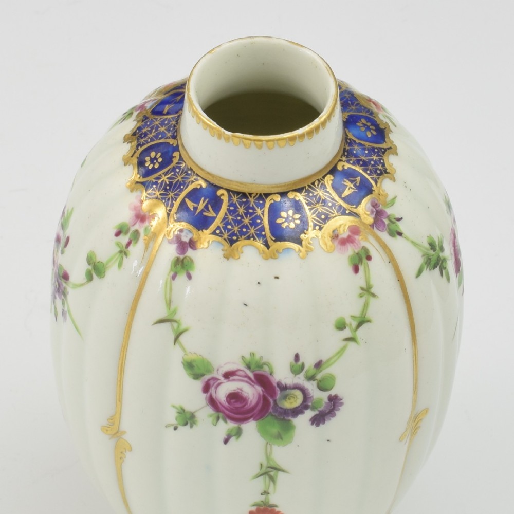 An 18th-century fluted white porcelain tea canister decorated with hand-painted floral swags, gilded trim, and a cobalt blue pattern around the neck. View XI