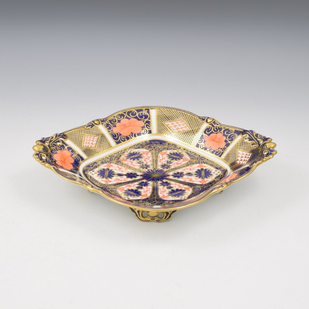 A shallow hexagonal bone china dish decorated in rich cobalt blue, iron red, and gold gilding, featuring pierced side handles and a footed base.
