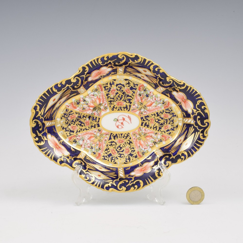 An oval antique Royal Crown Derby porcelain serving dish featuring intricate cobalt blue, coral red, and heavy gold leaf Imari pattern 6299 details with a lobed edge. View IV