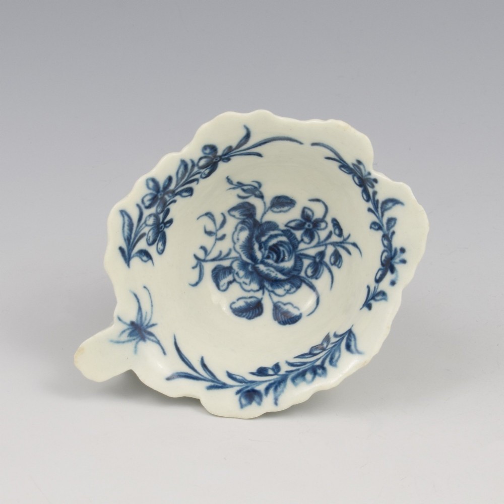 A leaf-shaped soft-paste porcelain butter boat decorated with an underglaze blue hand-painted rose motif and a floral running border.