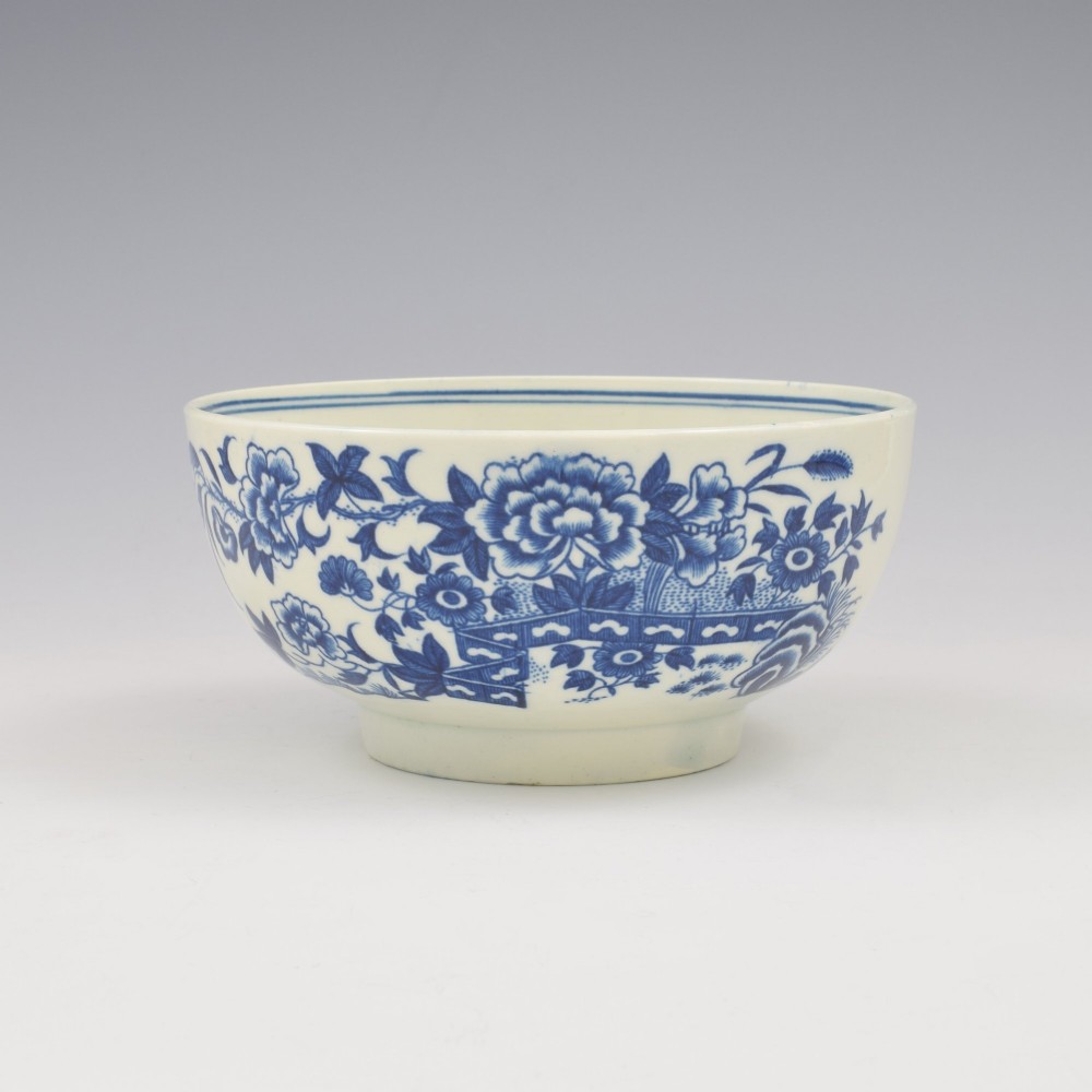 An 18th-century blue and white soft-paste porcelain slop bowl decorated with the oriental fence pattern and floral motifs.