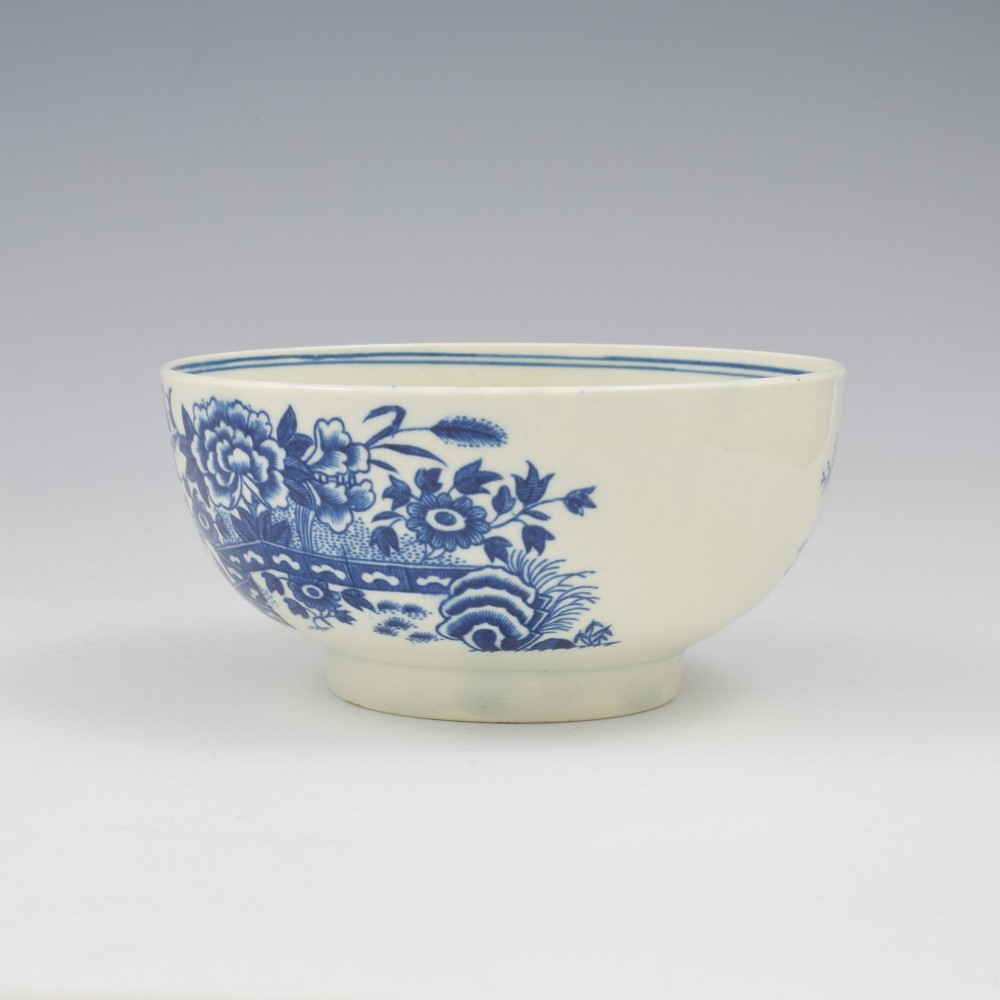 An 18th-century blue and white soft-paste porcelain slop bowl decorated with the oriental fence pattern and floral motifs. View V