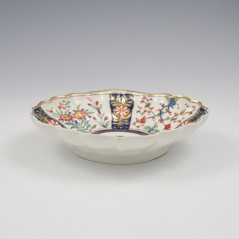 An 18th-century circular soft-paste porcelain dish with a scalloped rim, decorated in the Rich Queens pattern featuring cobalt blue gilt panels alternating with painted red and green floral motifs. View III