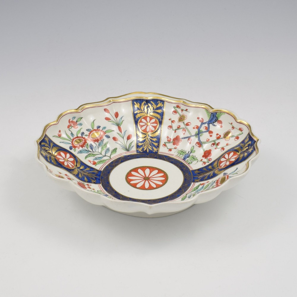An 18th-century circular soft-paste porcelain dish with a scalloped rim, decorated in the Rich Queens pattern featuring cobalt blue gilt panels alternating with painted red and green floral motifs. View IV