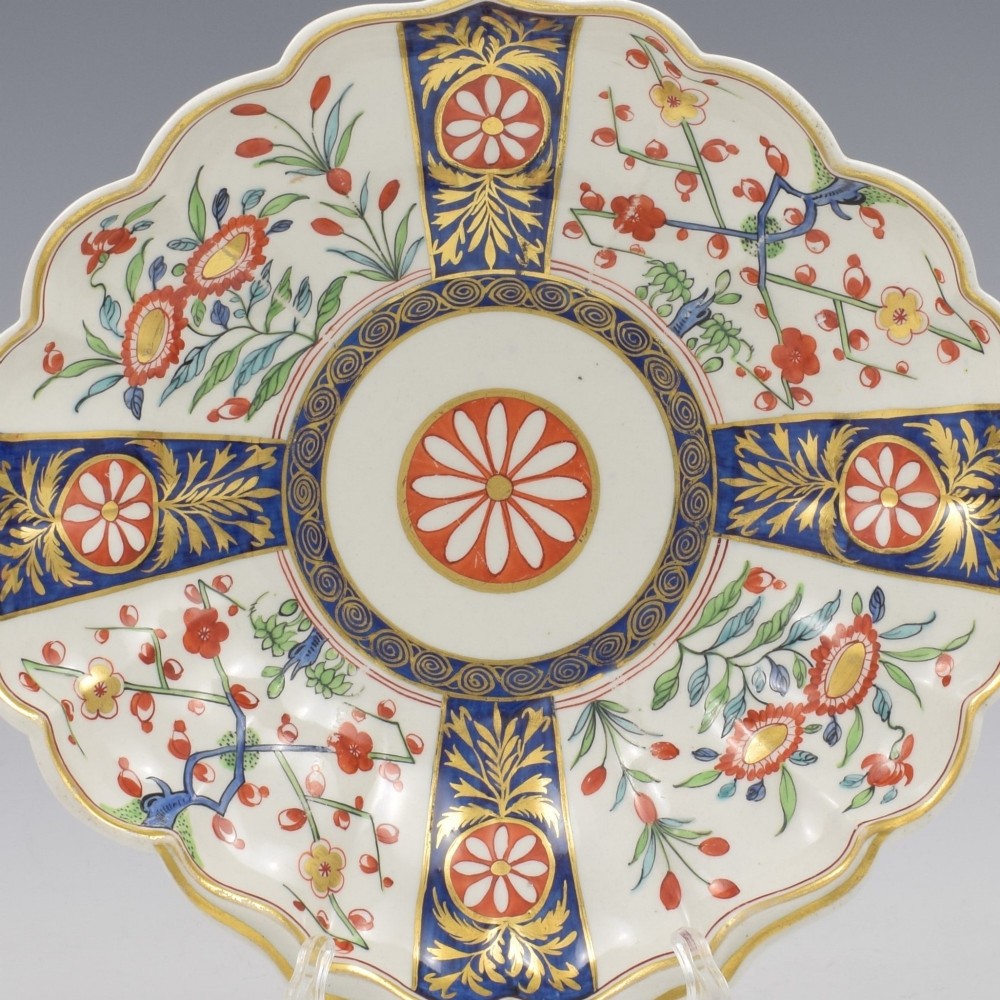 An 18th-century circular soft-paste porcelain dish with a scalloped rim, decorated in the Rich Queens pattern featuring cobalt blue gilt panels alternating with painted red and green floral motifs. View V