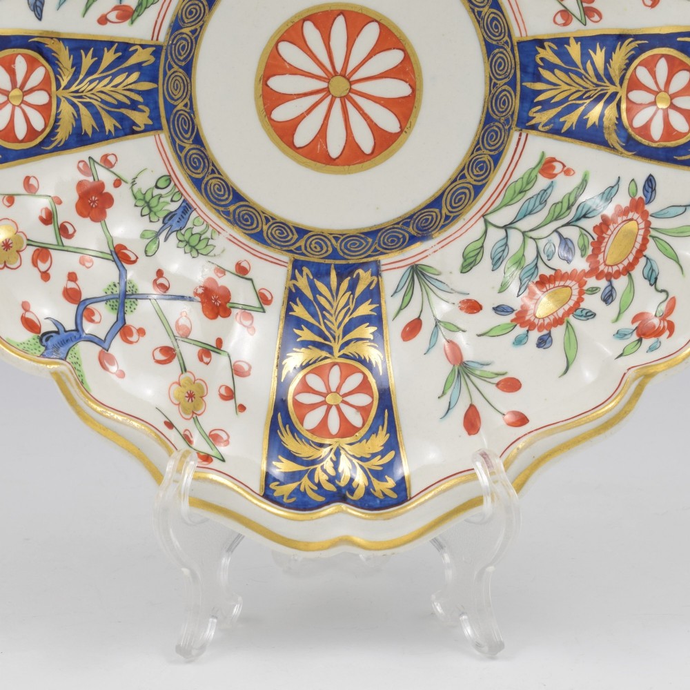 An 18th-century circular soft-paste porcelain dish with a scalloped rim, decorated in the Rich Queens pattern featuring cobalt blue gilt panels alternating with painted red and green floral motifs. View VI