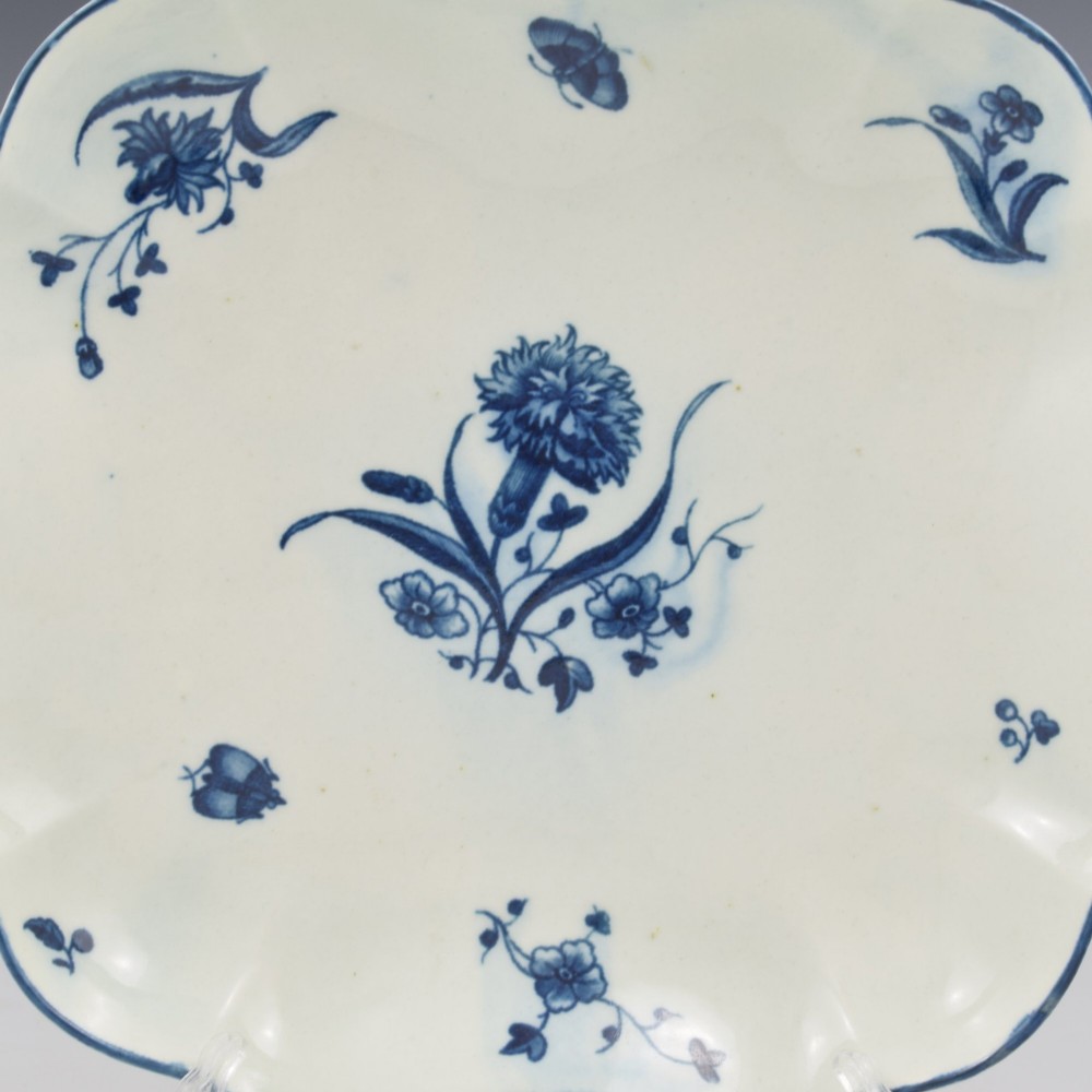 A square soft-paste porcelain dessert dish with scalloped edges, decorated in underglaze blue with a central carnation motif and surrounding floral sprigs. View II