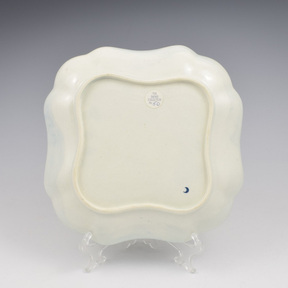 A square soft-paste porcelain dessert dish with scalloped edges, decorated in underglaze blue with a central carnation motif and surrounding floral sprigs. View III