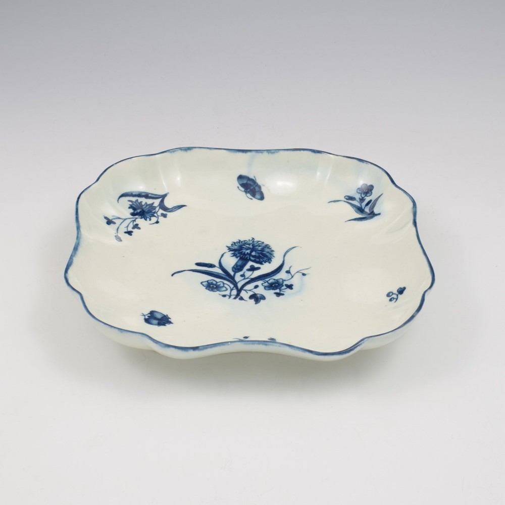 A square soft-paste porcelain dessert dish with scalloped edges, decorated in underglaze blue with a central carnation motif and surrounding floral sprigs. View IV