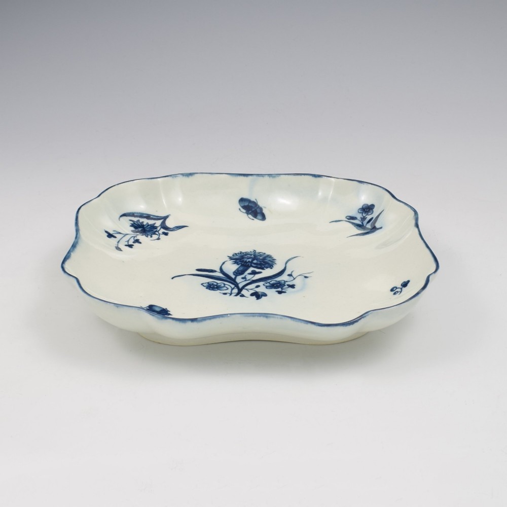 A square soft-paste porcelain dessert dish with scalloped edges, decorated in underglaze blue with a central carnation motif and surrounding floral sprigs. View V