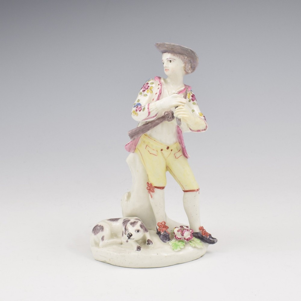 An eighteenth-century Bow porcelain figurine depicting a young shepherd playing a pipe alongside a small dog on a sculpted base.