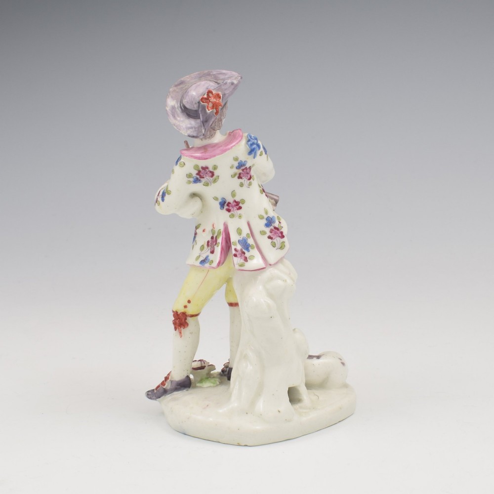 An eighteenth-century Bow porcelain figurine depicting a young shepherd playing a pipe alongside a small dog on a sculpted base. View V