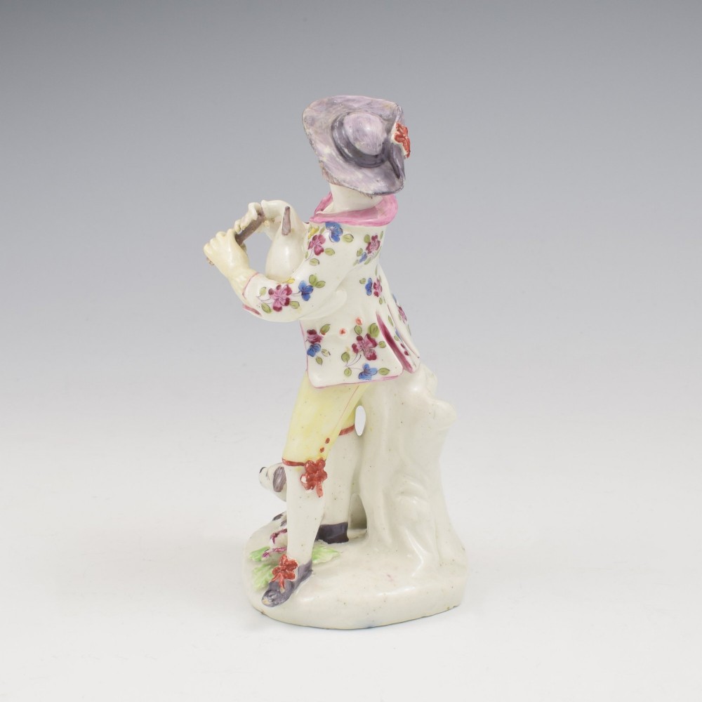 An eighteenth-century Bow porcelain figurine depicting a young shepherd playing a pipe alongside a small dog on a sculpted base. View VII