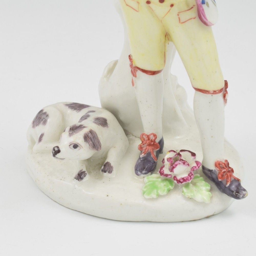 An eighteenth-century Bow porcelain figurine depicting a young shepherd playing a pipe alongside a small dog on a sculpted base. View XII