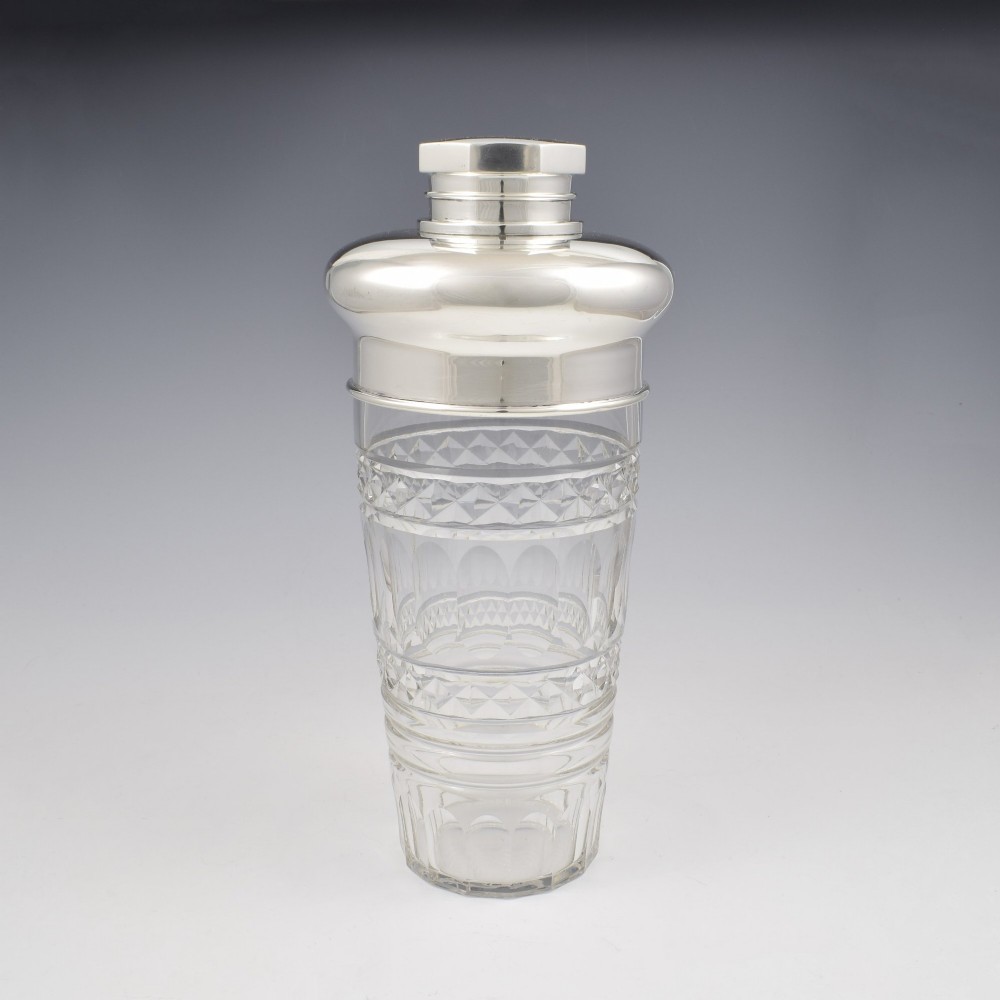 An Art Deco cocktail shaker featuring a clear cut glass body with geometric facet patterns and a polished sterling silver mount and octagonal cap. View II