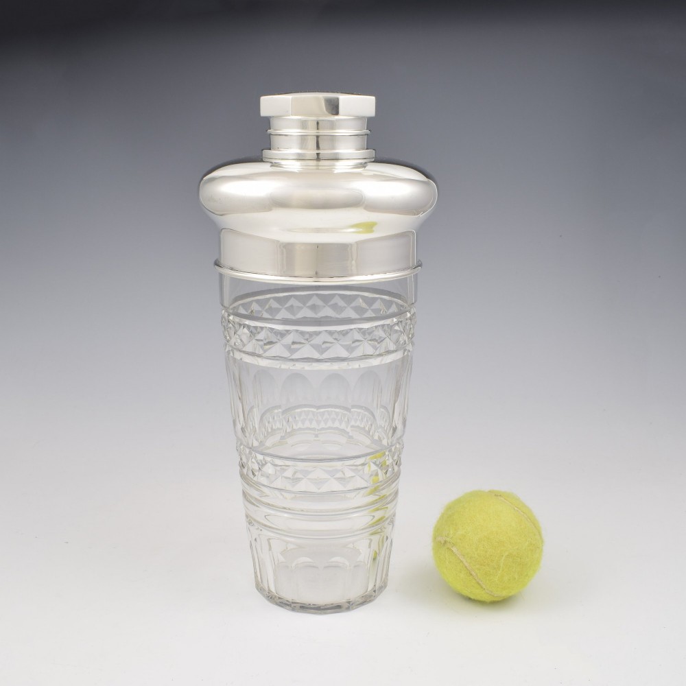 An Art Deco cocktail shaker featuring a clear cut glass body with geometric facet patterns and a polished sterling silver mount and octagonal cap. View III