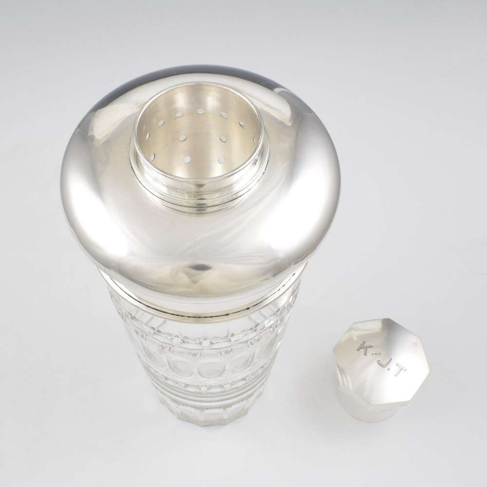 An Art Deco cocktail shaker featuring a clear cut glass body with geometric facet patterns and a polished sterling silver mount and octagonal cap. View VI