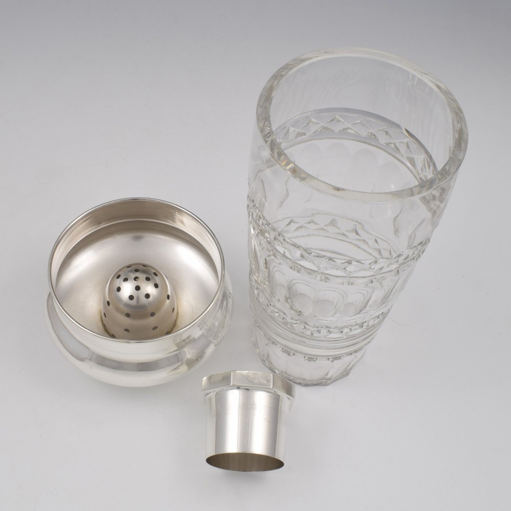 An Art Deco cocktail shaker featuring a clear cut glass body with geometric facet patterns and a polished sterling silver mount and octagonal cap. View VII