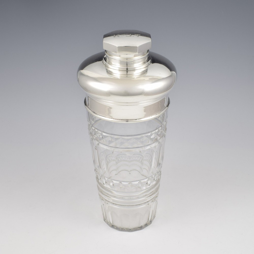 An Art Deco cocktail shaker featuring a clear cut glass body with geometric facet patterns and a polished sterling silver mount and octagonal cap. View IX
