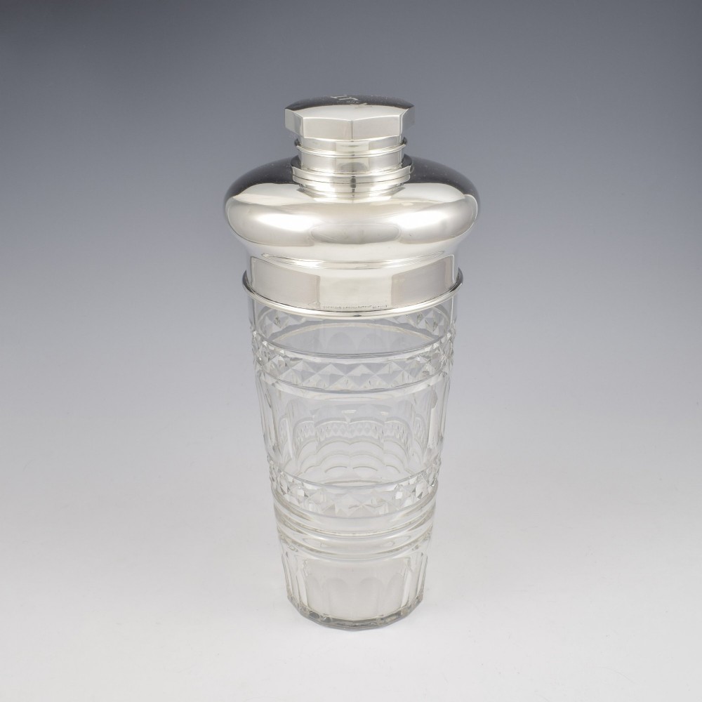An Art Deco cocktail shaker featuring a clear cut glass body with geometric facet patterns and a polished sterling silver mount and octagonal cap. View XII