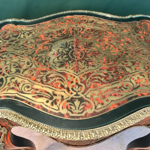fig 1. A French Napoleon III serpentine centre table featuring brass and red tortoiseshell Boulle marquetry, cabriole legs, gilt bronze mounts, and a protective glass top.
