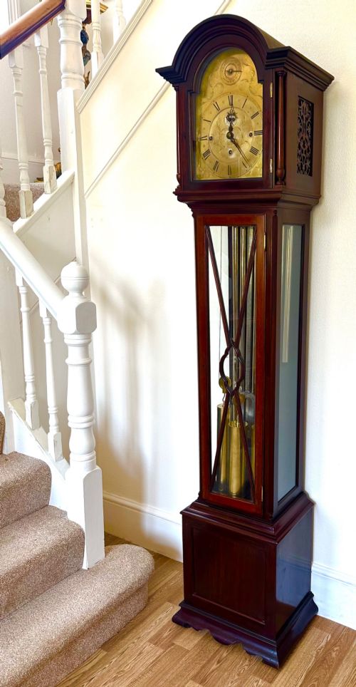 fig 1. An Edwardian mahogany longcase clock featuring an arched pediment, a brass dial with chime selectors, and a glazed door revealing polished brass weights and tubular bells.