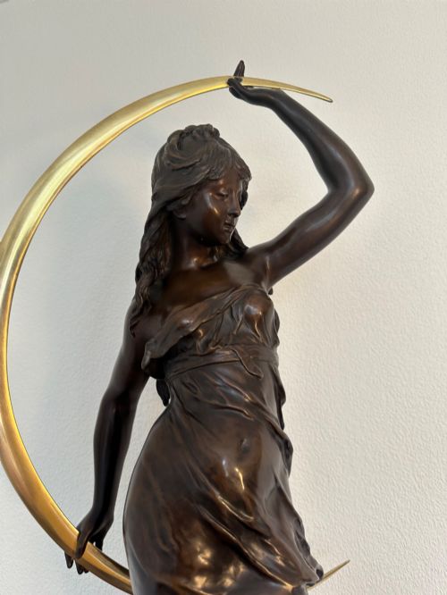 fig 2. A dark bronze sculpture depicting a draped female figure standing atop a starry globe and mounted on a dark red marble base.