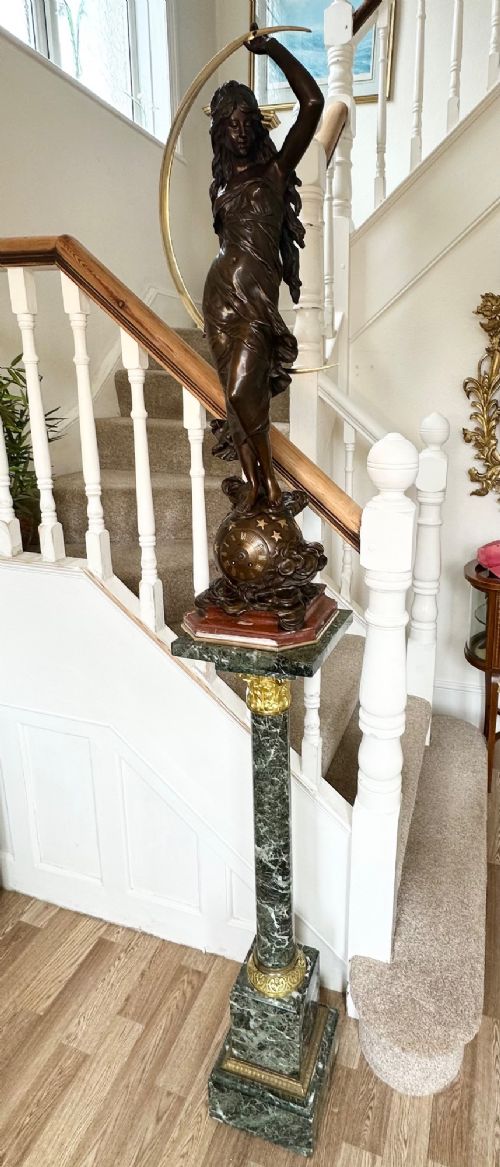A dark bronze sculpture depicting a draped female figure standing atop a starry globe and mounted on a dark red marble base. View IV