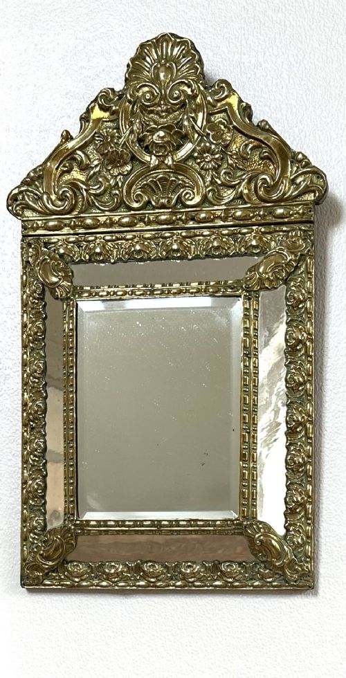 An antique repousse brass marginal mirror featuring an ornate floral pediment crest and bevelled glass borders. View VI