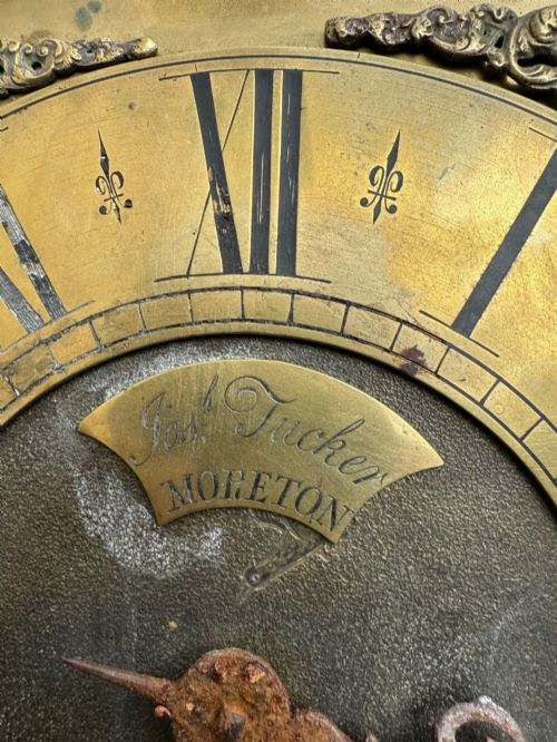 fig 1. A square eighteenth-century brass clock dial with cast corner spandrels, Roman numerals, engraved centre detailing, and rusty iron chains.