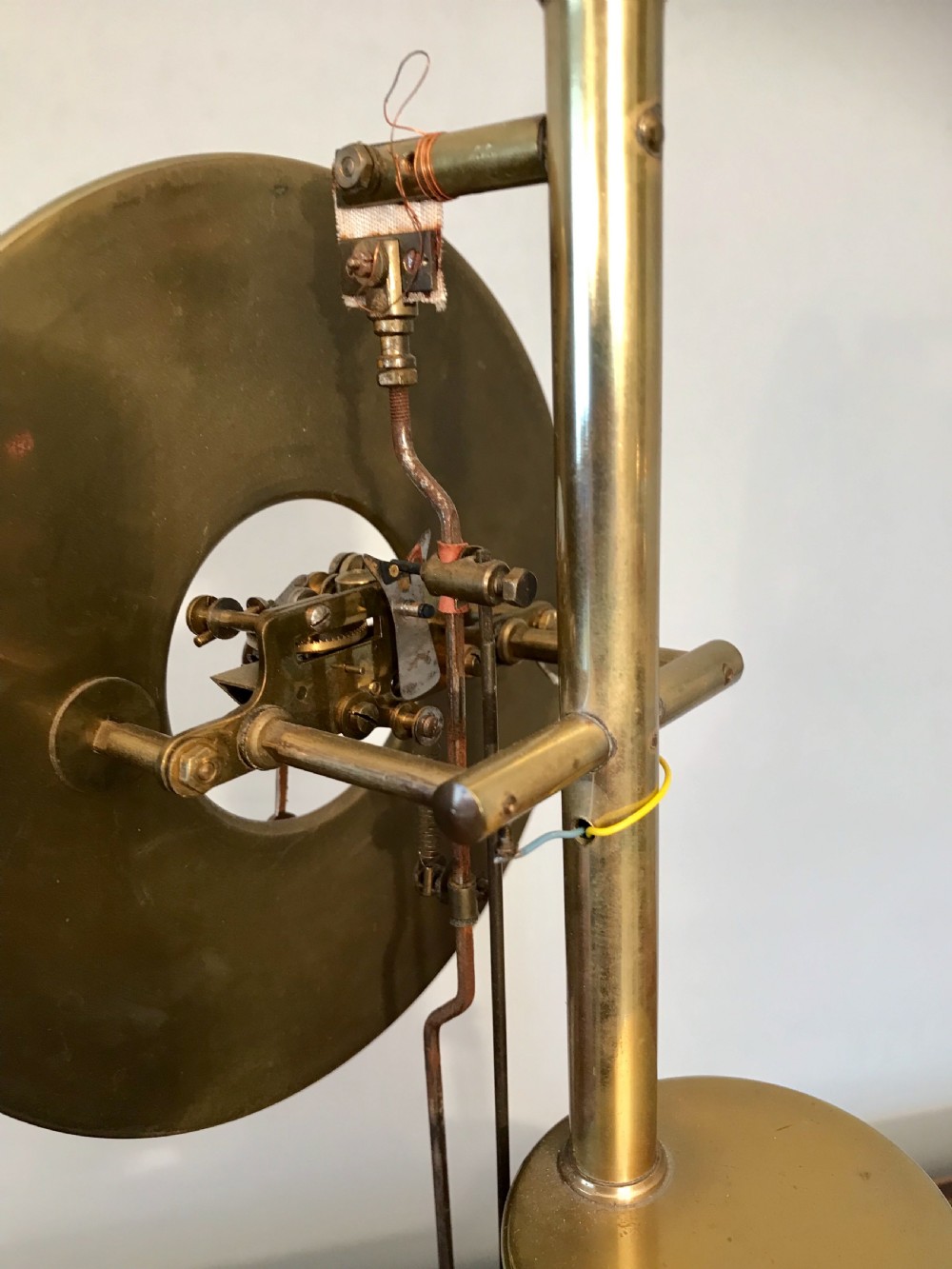 An antique Bulle electric clock displaying an open brass movement with a white dial, enclosed beneath a tall clear glass dome on a wooden base. View V