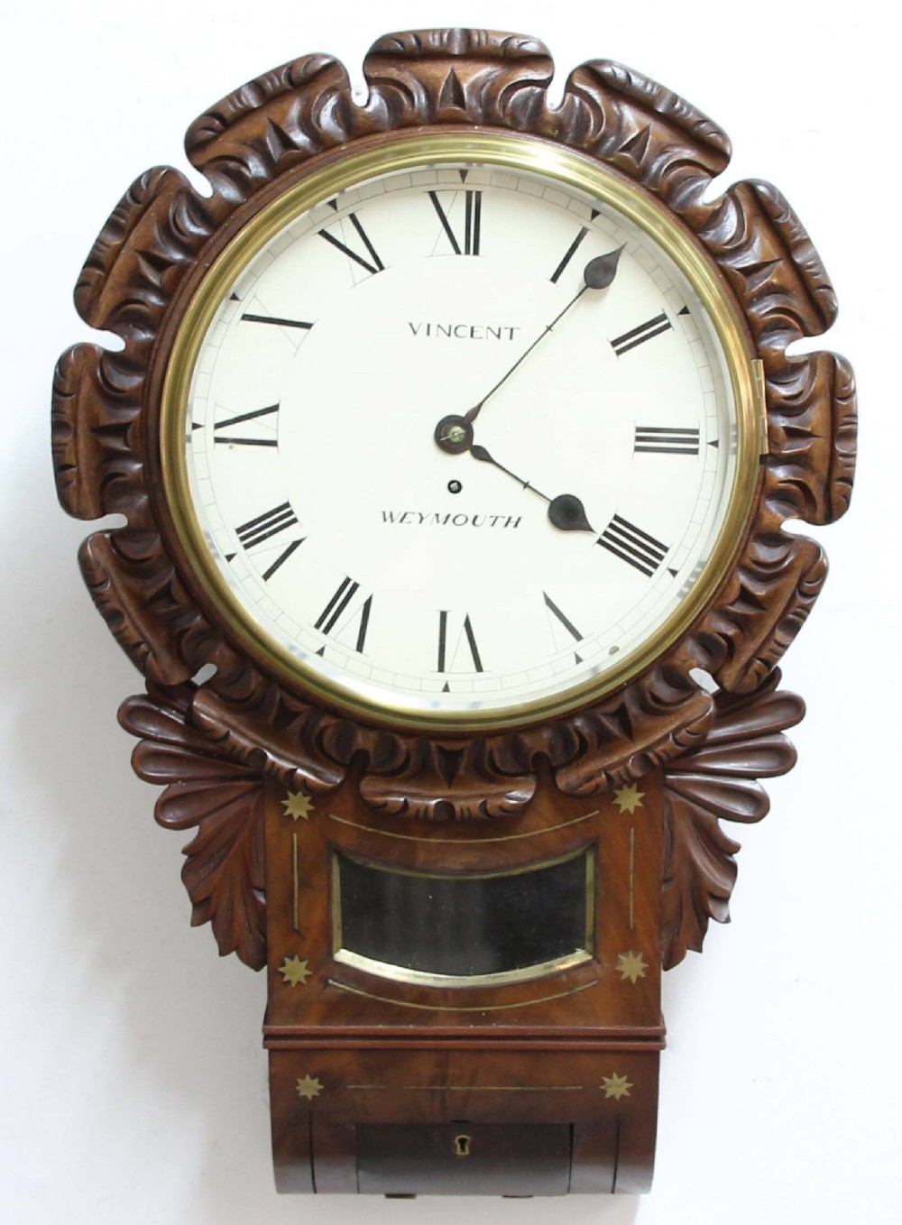 An antique Regency mahogany wall clock featuring a carved acanthus bezel frame, brass star inlay on the drop case, and a white dial with Roman numerals.