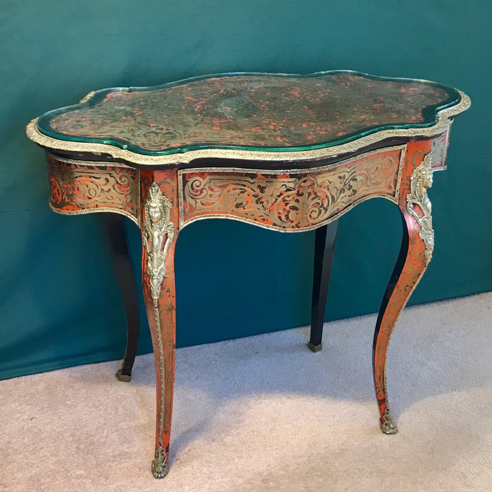 A French Napoleon III serpentine centre table featuring brass and red tortoiseshell Boulle marquetry, cabriole legs, gilt bronze mounts, and a protective glass top.