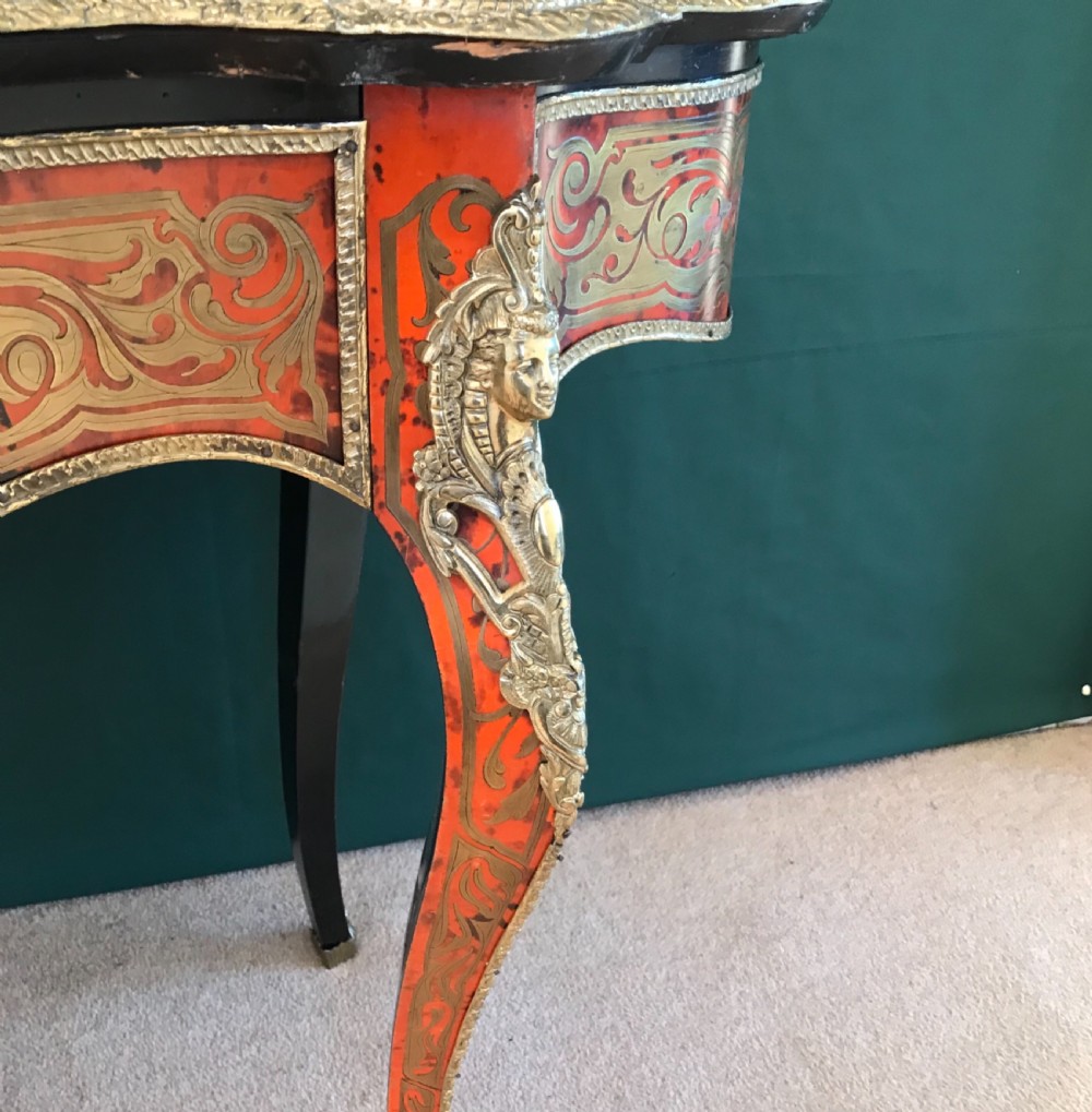 A French Napoleon III serpentine centre table featuring brass and red tortoiseshell Boulle marquetry, cabriole legs, gilt bronze mounts, and a protective glass top. View VI