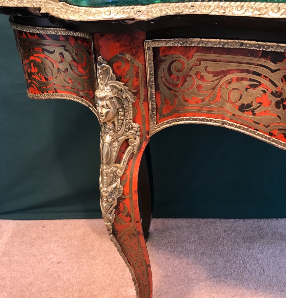 A French Napoleon III serpentine centre table featuring brass and red tortoiseshell Boulle marquetry, cabriole legs, gilt bronze mounts, and a protective glass top. View VIII