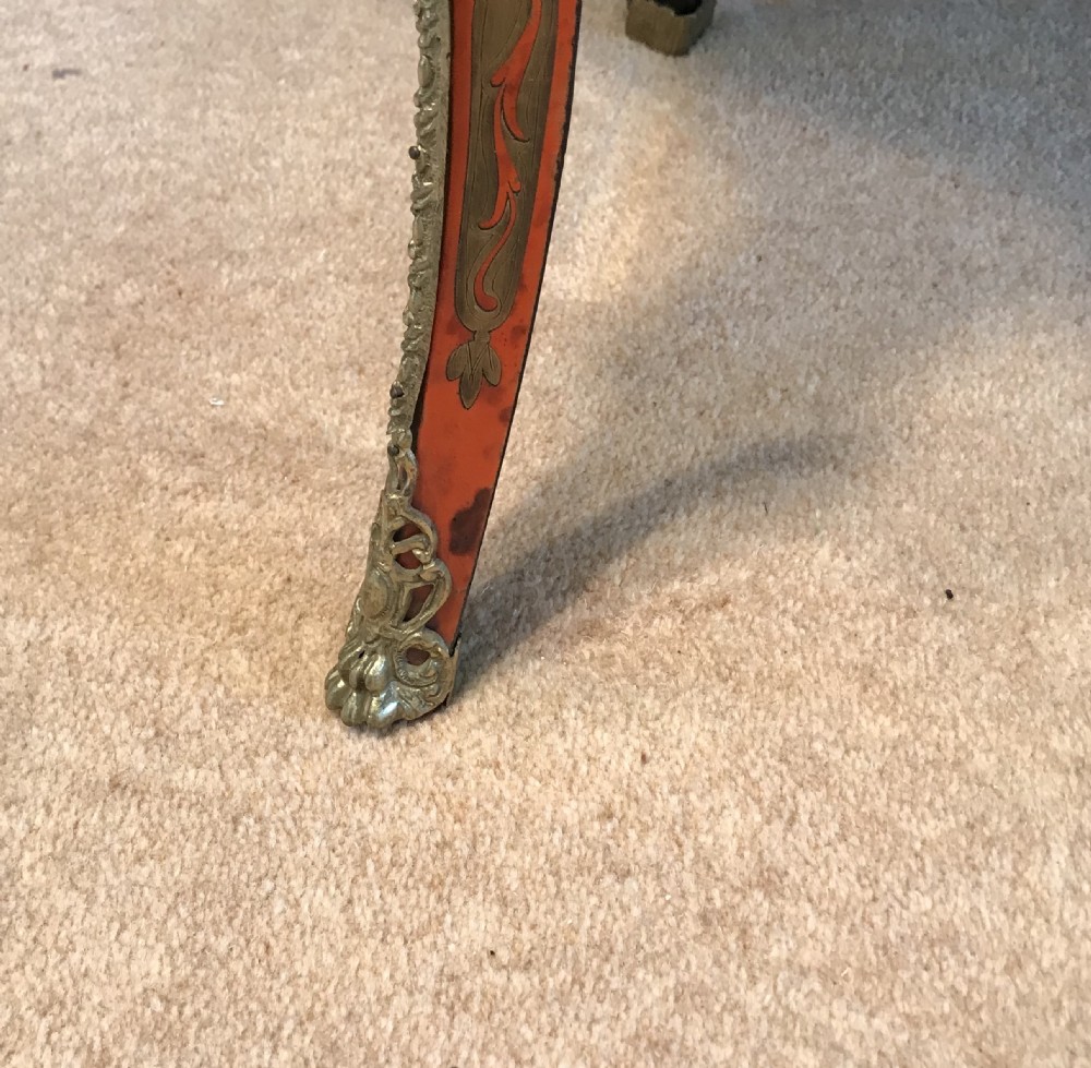 A French Napoleon III serpentine centre table featuring brass and red tortoiseshell Boulle marquetry, cabriole legs, gilt bronze mounts, and a protective glass top. View IX