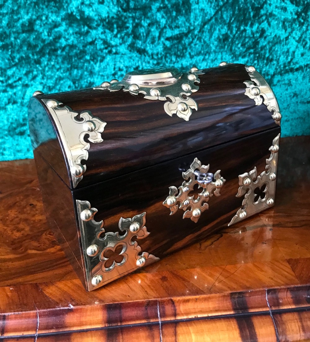 A Victorian dome-topped wooden box crafted from dark timber featuring decorative pierced brass strapwork and a key inserted in the lock.