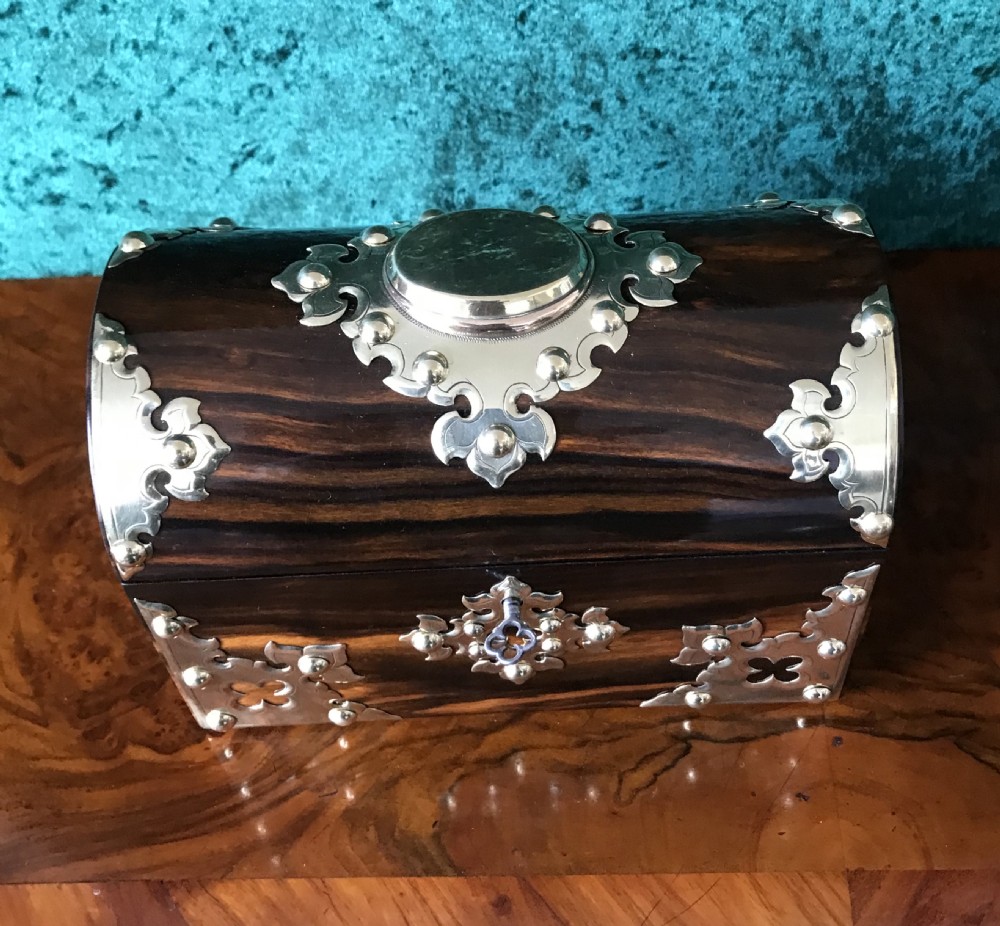 A Victorian dome-topped wooden box crafted from dark timber featuring decorative pierced brass strapwork and a key inserted in the lock. View II