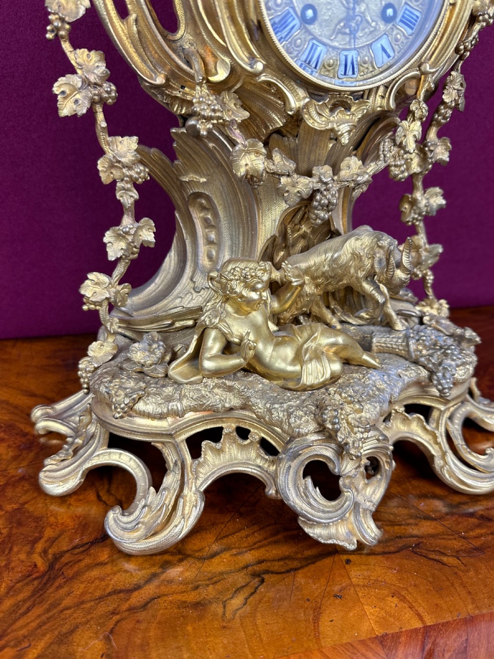 An ornate 19th-century French gilt bronze mantel clock featuring sculptural cherubs, grapevine garlands, and an enamel Roman numeral dial face. View II