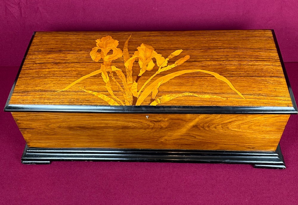 A rectangular Victorian wooden music box featuring floral iris marquetry inlaid on the lid with ebonised moulded borders.
