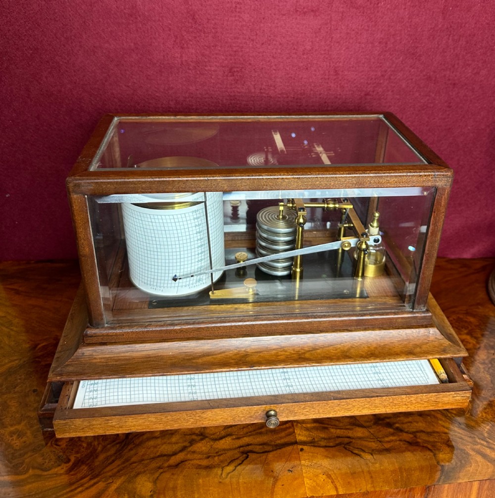 A late Victorian walnut cased barograph featuring a brass mechanism, paper chart drum, and a lower drawer containing graph papers, visible through a glass display hood.