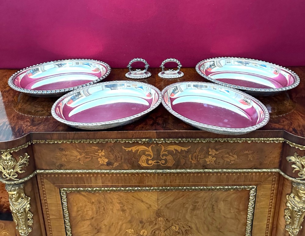 A pair of oval silver-plated entree dishes with beaded rims, engraved lids, and detachable handles, displayed on a burr wood surface. View III