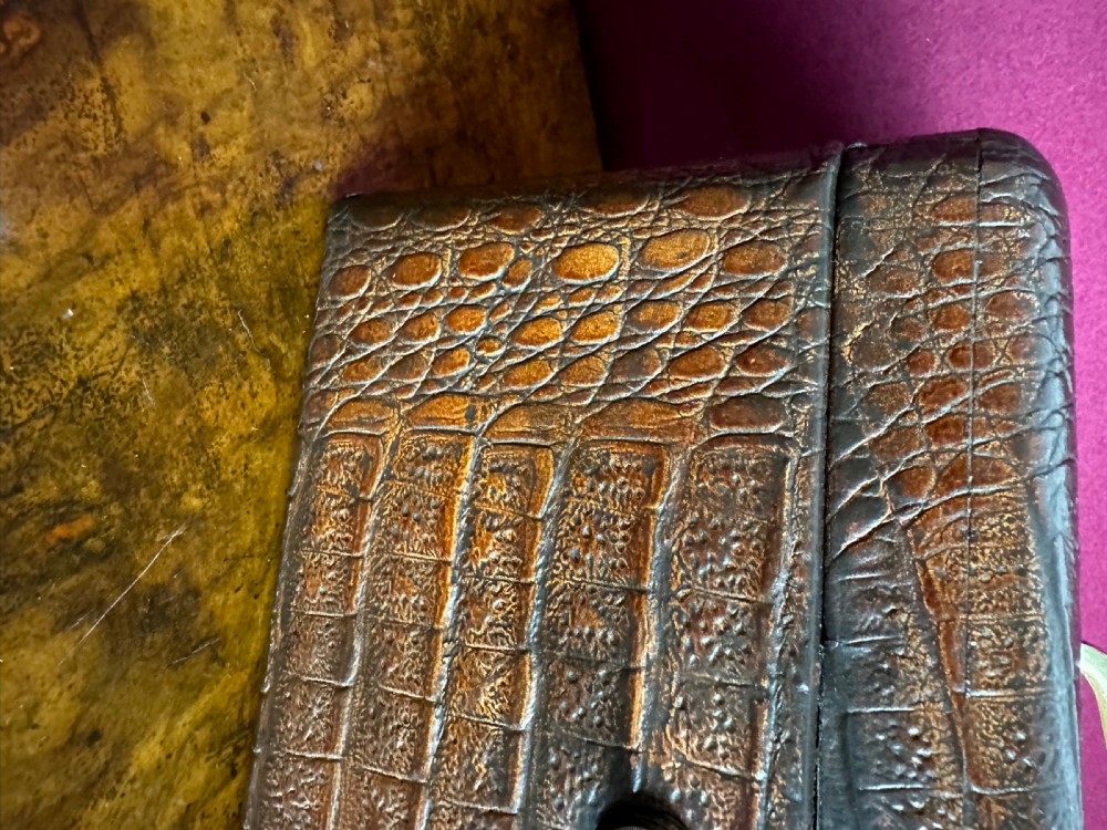 A rectangular dark brown crocodile leather jewellery box shown open, displaying a bright blue velvet interior lining and a metal key inserted into the front lock. View III