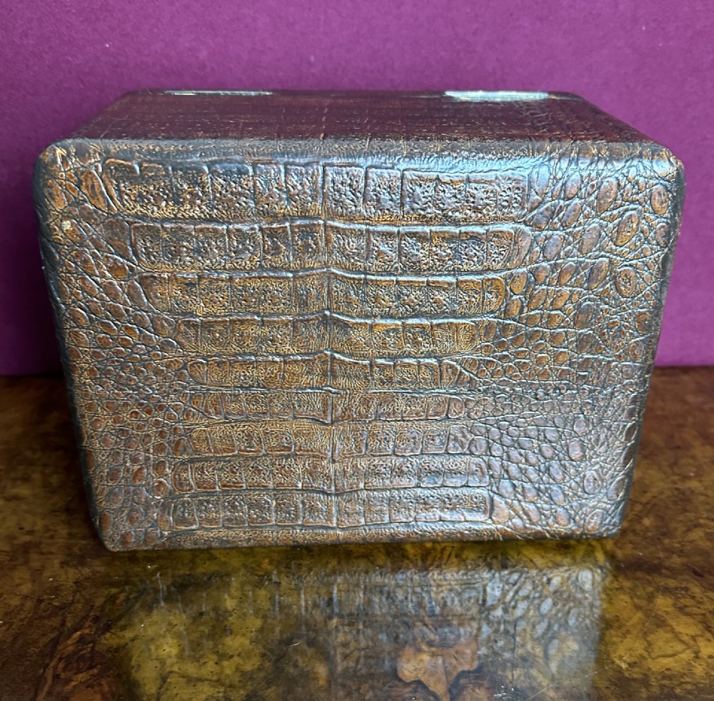 A rectangular dark brown crocodile leather jewellery box shown open, displaying a bright blue velvet interior lining and a metal key inserted into the front lock. View VI